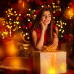 Beautiful dreamy girl sits with a gift box in the fairy Christmas interior with lights around.